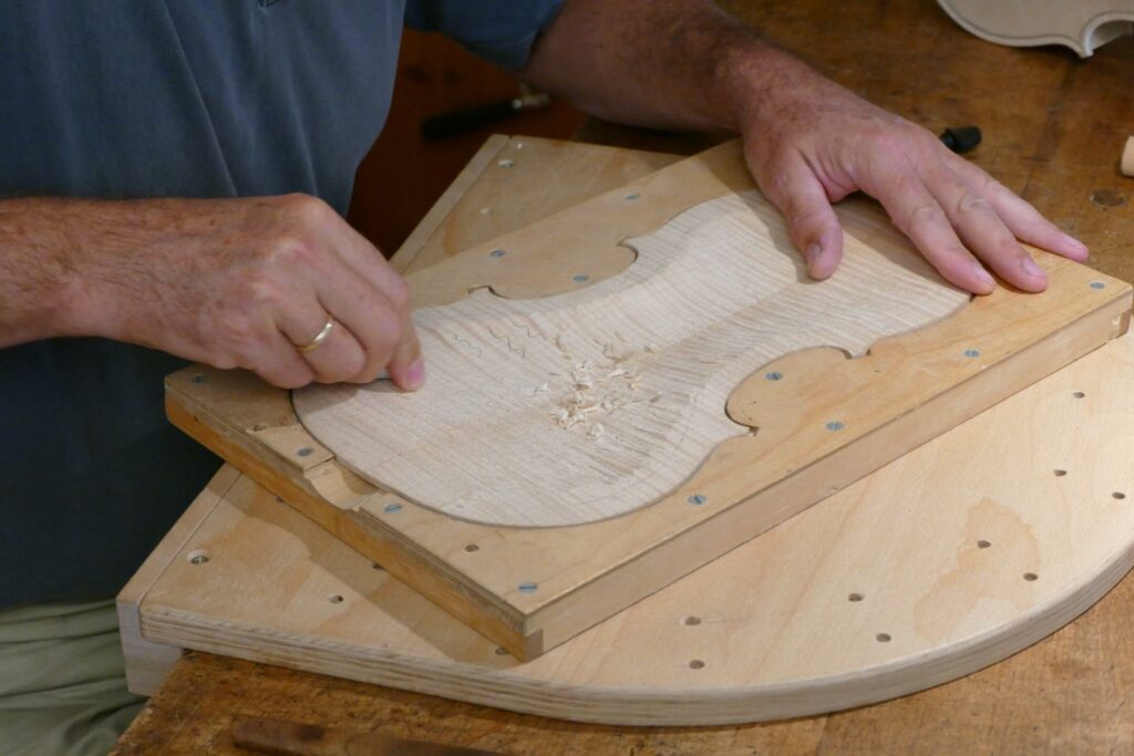 Primer plano de las manos de un luthier trabajando en el cuerpo de una guitarra española de madera.